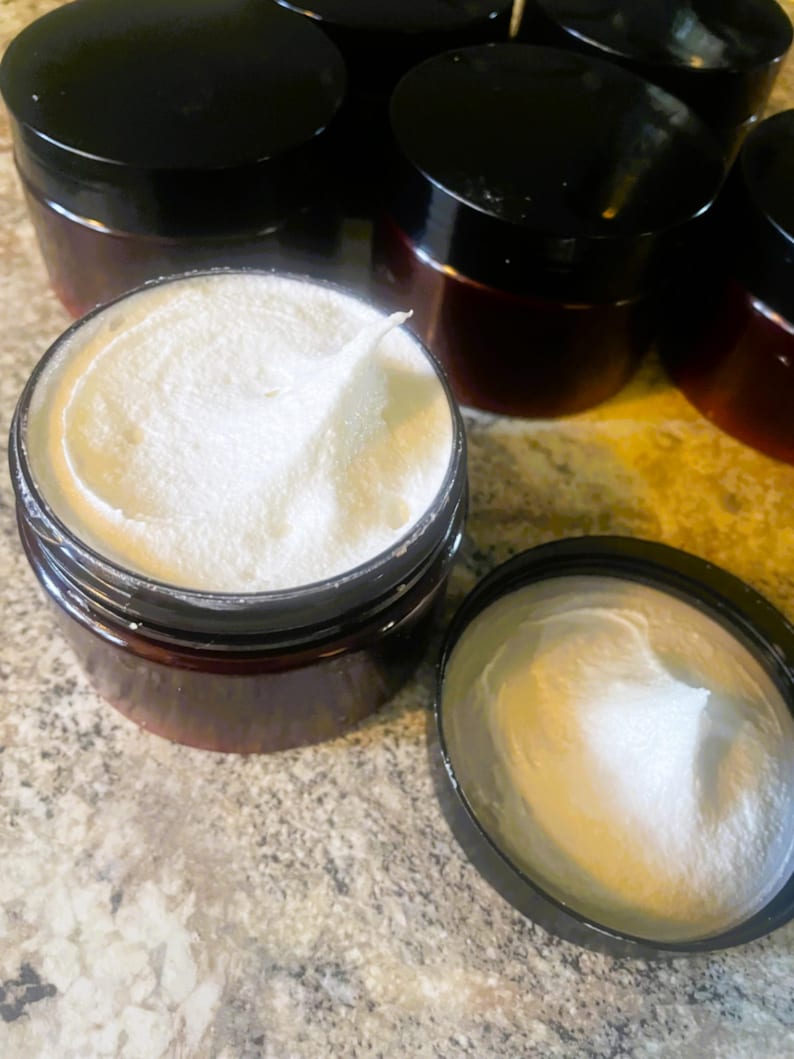 Puede incluir: Varios frascos peque&ntilde;os de color marr&oacute;n oscuro con tapas negras, llenos de una sustancia cremosa blanca. Un frasco est&aacute; abierto, revelando la textura del producto. Los frascos est&aacute;n dispuestos sobre una superficie clara.