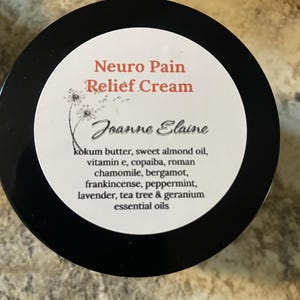 Puede incluir: Un frasco negro con una etiqueta blanca con el texto "Neuro Pain Relief Cream" en rojo. La etiqueta tambi&eacute;n incluye el nombre "Joanne Elaine" y una lista de ingredientes, incluidos aceites esenciales.