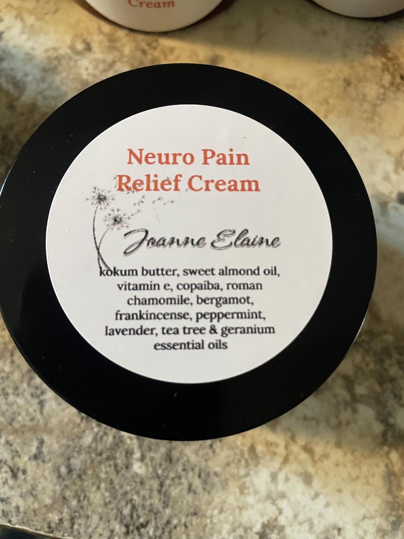 Puede incluir: Un frasco negro con una etiqueta blanca con el texto "Neuro Pain Relief Cream" en rojo. La etiqueta tambi&eacute;n incluye el nombre "Joanne Elaine" y una lista de ingredientes, incluidos aceites esenciales.
