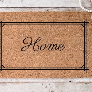 May include: A brown coir doormat with a black frame and the word "Home" in a cursive font.