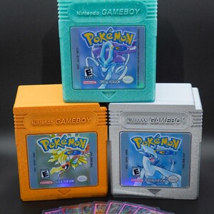 Puede incluir: Tres cartuchos de juego Game Boy Color vintage para la serie de videojuegos Pokemon. Los cartuchos est&aacute;n en sus estuches originales y son de color turquesa, naranja y plateado. Los cartuchos est&aacute;n etiquetados como "Pokemon Crystal Version", "Pokemon Gold Version" y "Pokemon Silver Version".