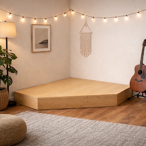 Könnte beinhalten: Ein Eck-Plattform-Bettrahmen aus hellem Holz. Der Raum verfügt über eine Gitarre, eine Topfpflanze, einen Weidenkorb, eine Stehlampe und eine Lichterkette. Die Plattform ist etwa 183 cm breit und 183 cm lang.