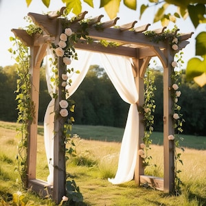 Puede incluir: Arco de boda de madera adornado con rosas blancas, vides verdes y cortinas de tela blanca fluida. El arco se encuentra en un campo de hierba con árboles al fondo, creando un ambiente romántico al aire libre.