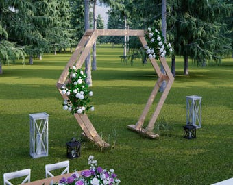 May include: A wooden wedding arch decorated with white flowers and greenery stands on a grassy lawn. Two white lanterns and two black lanterns are placed nearby. A table with white chairs and floral arrangements is in the foreground.