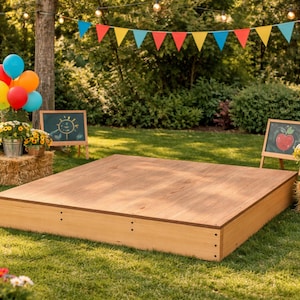 Peut inclure: Une scène en bois installée à l'extérieur sur une pelouse, décorée pour une fête. Des ballons colorés, des guirlandes de fanions et de petits tableaux noirs avec des dessins ajoutent à l'ambiance festive. Des bottes de foin et des fleurs en pot sont également présentes.