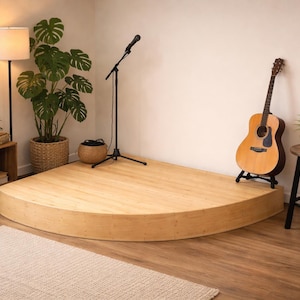 May include: A light wood stage with a microphone stand, guitar, and potted plants. A floor lamp and a small wooden side table are also present. The stage is semi-circular and has a natural wood finish. The room has a neutral color palette.