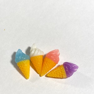 May include: Four miniature ice cream cones with different colored ice cream. The cones are yellow and white, and the ice cream is blue, pink, white, and purple.