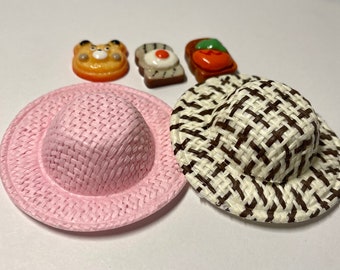 May include: Two miniature straw hats, one pink and one with a brown and white checkered pattern.