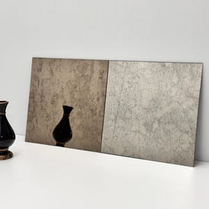May include: A black ceramic vase with a gold-colored base and rim stands in front of a two-panel textured backdrop. The vase has a glossy finish and a classic, elegant shape. The backdrop has a neutral color palette.