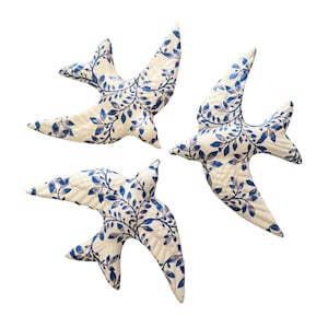 Pode incluir: Três pássaros de cerâmica branca com um padrão floral azul e branco. Os pássaros estão em voo e olham para direções diferentes.