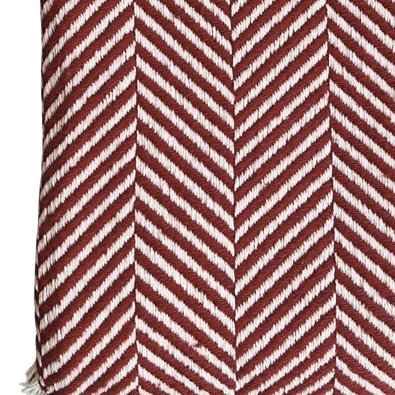 May include: A textile fabric featuring a prominent herringbone pattern in alternating stripes of deep brick red and off-white. The woven material displays a consistent diagonal texture throughout, creating a repeating chevron design across the surface.
