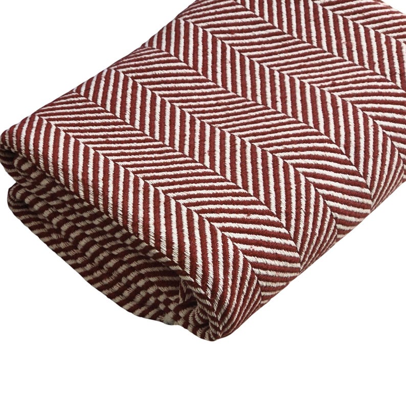May include: A folded textile featuring a prominent herringbone pattern in deep burgundy red and off-white. The fabric displays a dense, woven texture with alternating diagonal lines that create a consistent zigzag visual effect across the surface.