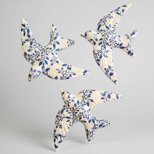 May include: Three ceramic bird wall decorations in a flying pose. Each piece features an off-white base colour with a detailed blue botanical leaf and vine pattern covering the surface. The birds are depicted with wings spread in flight.