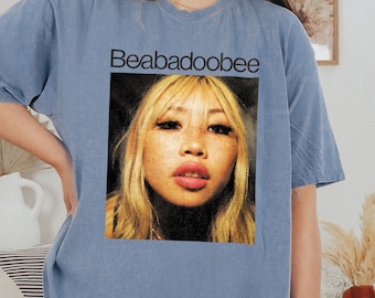 May include: A light blue oversized t-shirt with a graphic print of a woman's face and the text "Beabadoobee" in black.