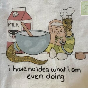 Op de afbeelding: Illustratie van een slangkok met een koksmuts, omringd door bakbenodigdheden: melkpak, suikerzak, mengkom en maatbeker. De tekst "i have no idea what i am even doing" staat onderaan.