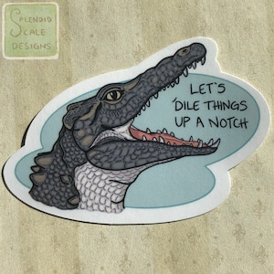May include: A sticker featuring a cartoon crocodile with an open mouth and the text "Let's Dille Things Up A Notch". The crocodile is gray and white with a blue background.