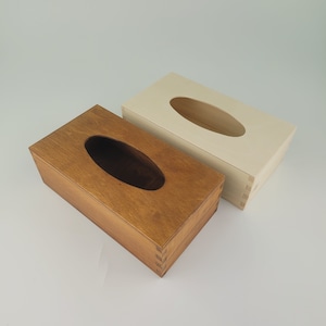 May include: Two wooden tissue box covers. One is a natural wood colour and the other is stained a dark brown. Both have a rectangular shape with an oval opening for tissues.