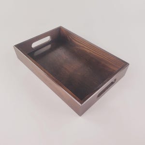May include: A dark brown wooden tray with two handles. The tray is empty and has a smooth surface.