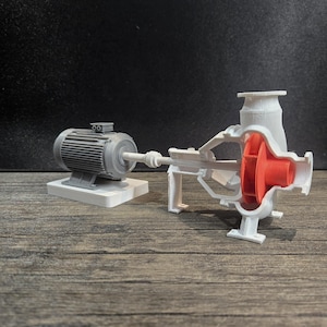 May include: A 3D-printed model of a pump, showcasing its internal components. The model features a gray electric motor on a white base, connected to a white pump housing with a visible red impeller. The model is displayed on a wooden surface.