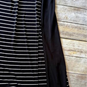 May include: A black and white striped dress with a solid black panel on the side. The dress has horizontal white stripes on a black background. The fabric appears to be soft and flowing.