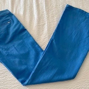 Pode incluir: Cal&ccedil;as azuis claras com design de perna larga. As cal&ccedil;as s&atilde;o feitas de um tecido liso e t&ecirc;m um design cl&aacute;ssico de cinco bolsos. As cal&ccedil;as est&atilde;o colocadas sobre uma superf&iacute;cie branca texturizada.