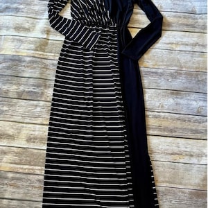 May include: A long maxi dress with a black and white striped pattern on the left side and a solid black panel on the right. The dress has long sleeves and a V-neck. The fabric appears soft.