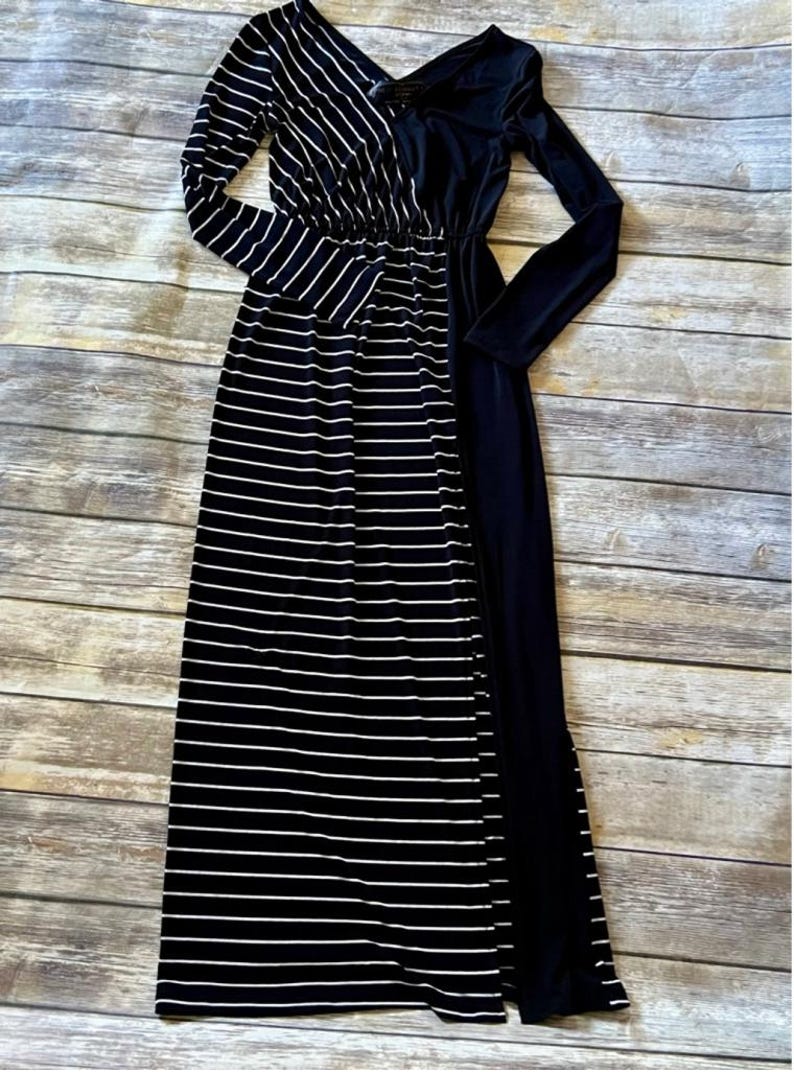 May include: A long maxi dress with a black and white striped pattern on the left side and a solid black panel on the right. The dress has long sleeves and a V-neck. The fabric appears soft.