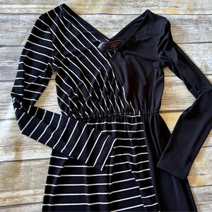 May include: A black and white striped maxi dress with a V-neck and long sleeves. The dress has a contrasting design, with one side featuring vertical white stripes on a black background and the other side solid black.