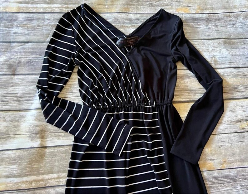 May include: A black and white striped maxi dress with a V-neck and long sleeves. The dress has a contrasting design, with one side featuring vertical white stripes on a black background and the other side solid black.