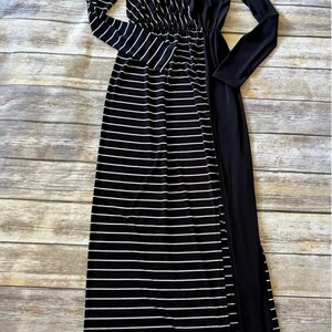 May include: A long maxi dress in black and white stripes, with long sleeves. The dress has a V-neck and a fitted waist. One side is solid black, the other striped. The fabric appears soft and flowing. The dress is suitable for various occasions.