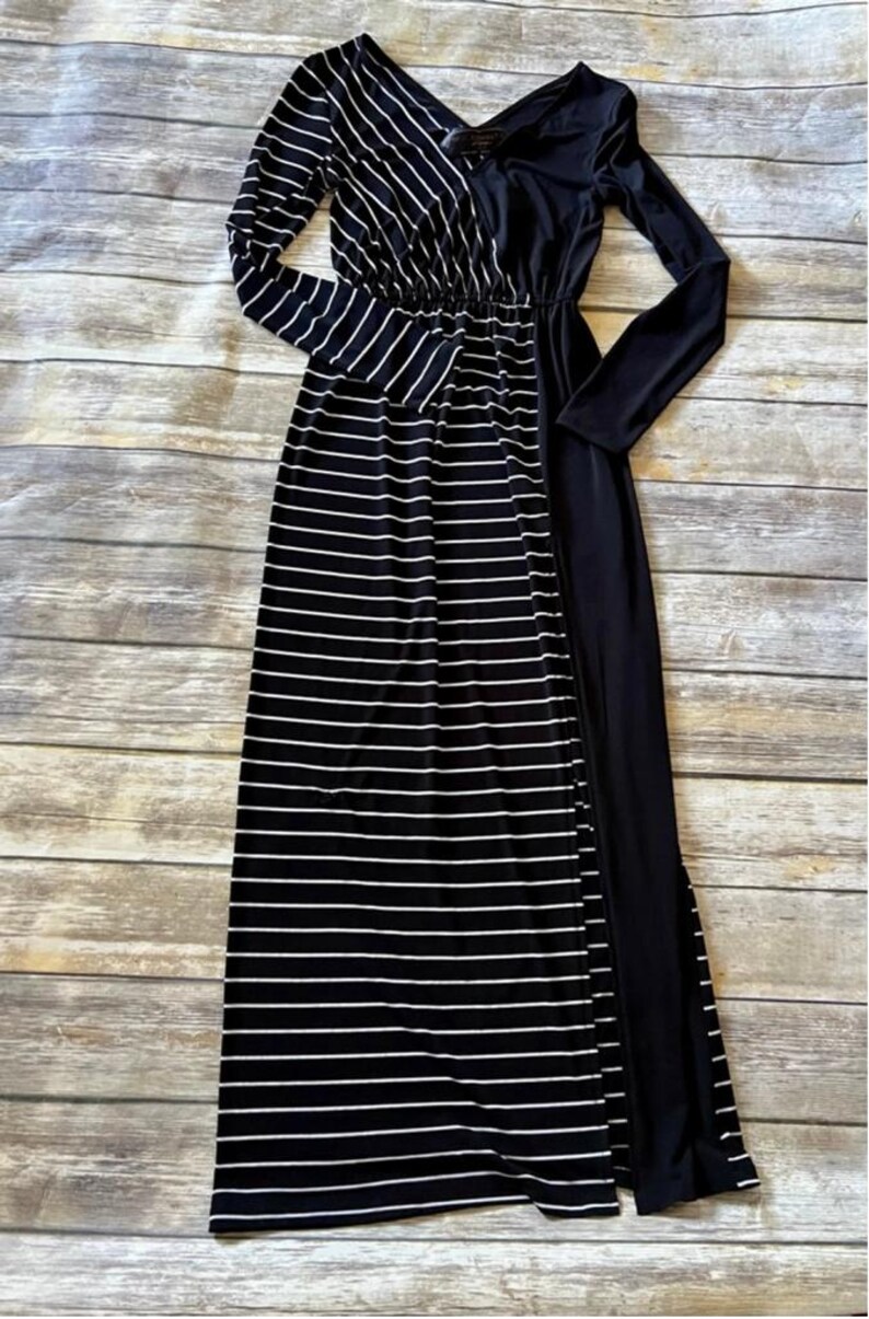 May include: A long maxi dress in black and white stripes, with long sleeves. The dress has a V-neck and a fitted waist. One side is solid black, the other striped. The fabric appears soft and flowing. The dress is suitable for various occasions.