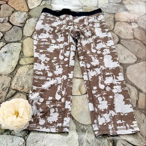 May include: Brown and white patterned athletic leggings with a black waistband. The leggings are cropped at the calf and feature a repeating abstract design. The fabric appears to be a stretchy material, suitable for workouts or casual wear.