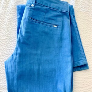 Pode incluir: Um par de cal&ccedil;as azuis claras dobradas. As cal&ccedil;as t&ecirc;m fecho de bot&atilde;o, um pequeno bolso nas costas e uma pequena etiqueta com o log&oacute;tipo. As cal&ccedil;as s&atilde;o feitas de um tecido texturizado e est&atilde;o cuidadosamente dobradas sobre uma superf&iacute;cie branca.