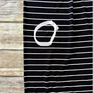 May include: Black and white striped fabric. The fabric features horizontal white stripes on a black background. The fabric is placed on a wooden surface. A white circle is drawn on the fabric, with a dark spot inside the circle.