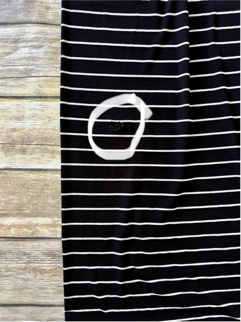 May include: Black and white striped fabric. The fabric features horizontal white stripes on a black background. The fabric is placed on a wooden surface. A white circle is drawn on the fabric, with a dark spot inside the circle.