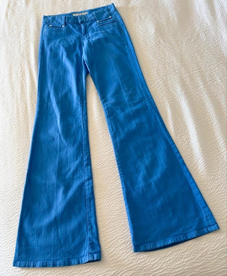 Pode incluir: Cal&ccedil;as de ganga azul brilhante com pernas largas. As cal&ccedil;as t&ecirc;m um design cl&aacute;ssico de cinco bolsos, fecho de bot&atilde;o e z&iacute;per e perna larga. O tecido parece ser ganga de peso m&eacute;dio. As cal&ccedil;as est&atilde;o estendidas numa superf&iacute;cie branca.