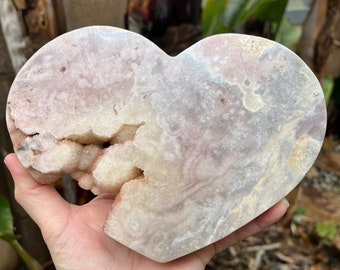 May include: A heart-shaped crystal with a pink and white color scheme. The crystal has a rough, natural texture and is partially hollow, revealing a white, crystalline interior.