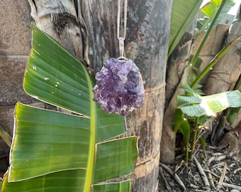 Colar com pingente de ametista roxa em formato de aglomerado e corrente prateada.
