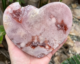 May include: A heart-shaped pink and white crystal with red and white inclusions. The crystal is polished and has a smooth surface.