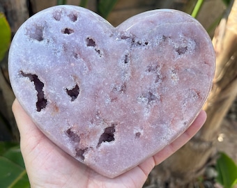 May include: A heart-shaped amethyst crystal with a light purple color and a natural, rough texture. The crystal has many small, hollow cavities throughout its surface.