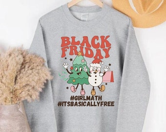 May include: A heather gray sweatshirt with a retro design featuring the text "BLACK FRIDAY" in orange and red. The graphic includes a cartoon Christmas tree and snowman. Below the graphic are the hashtags #GIRLMATH and #ITSBASICALLYFREE.