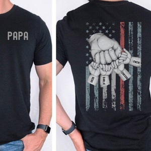 May include: Black t-shirt with the word "PAPA" on the front and an American flag design on the back. The flag design features a hand with four smaller hands holding onto it, each with a name: Owen, Carson,  Eaklie, and  Reid.
