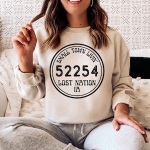 May include: A beige sweatshirt with a black circular graphic that says "Small Town Livin' 52254 Lost Nation IA".