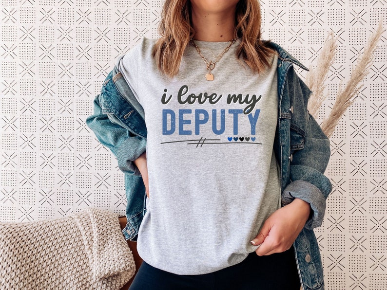 Pode incluir: Uma camiseta cinza com o texto "i love my DEPUTY" em letras azuis e pretas. H&aacute; quatro pequenos cora&ccedil;&otilde;es azuis abaixo do texto.