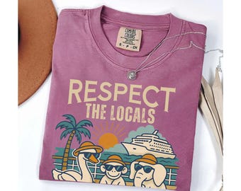 May include: A pink t-shirt with the text "Respect the Locals" in a retro font. The shirt features a cartoon illustration of a palm tree, a cruise ship, a goose, a monkey, and an elephant.