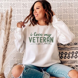 Pu&ograve; includere: Felpa bianca con il testo "i love my VETERAN" in lettere verdi con piccoli cuori verdi.