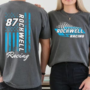 May include: Two gray t-shirts with racing-themed graphics. One shirt features a blue and white American flag design with the number 87 and "Rockwell Racing." The other shirt displays a checkered flag and the words "Rockwell Racing" in blue and white.