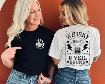 Op de afbeelding: Twee vrouwen dragen T-shirts. De vrouw links draagt een zwart T-shirt met een wit skelet-handontwerp en de tekst "Bride's Maid". De vrouw rechts draagt een wit T-shirt met de tekst "Whisky Bent & Veil Bound" in een vintage stijl.