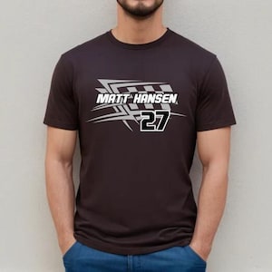 Może przedstawiać: Czarny t-shirt z białym nadrukiem przedstawiającym flagę w kratkę i tekst "MATT HANSEN 27".