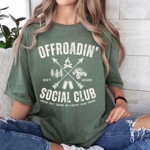 May include: A green t-shirt with a white graphic design that says "Offroadin' Social Club Est. 2025 Side by Side is How We Ride".